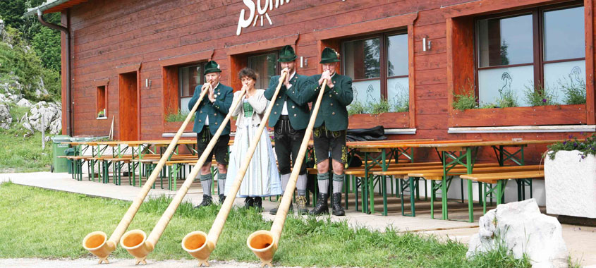 Vier Alphornbläser vor einer Hütte