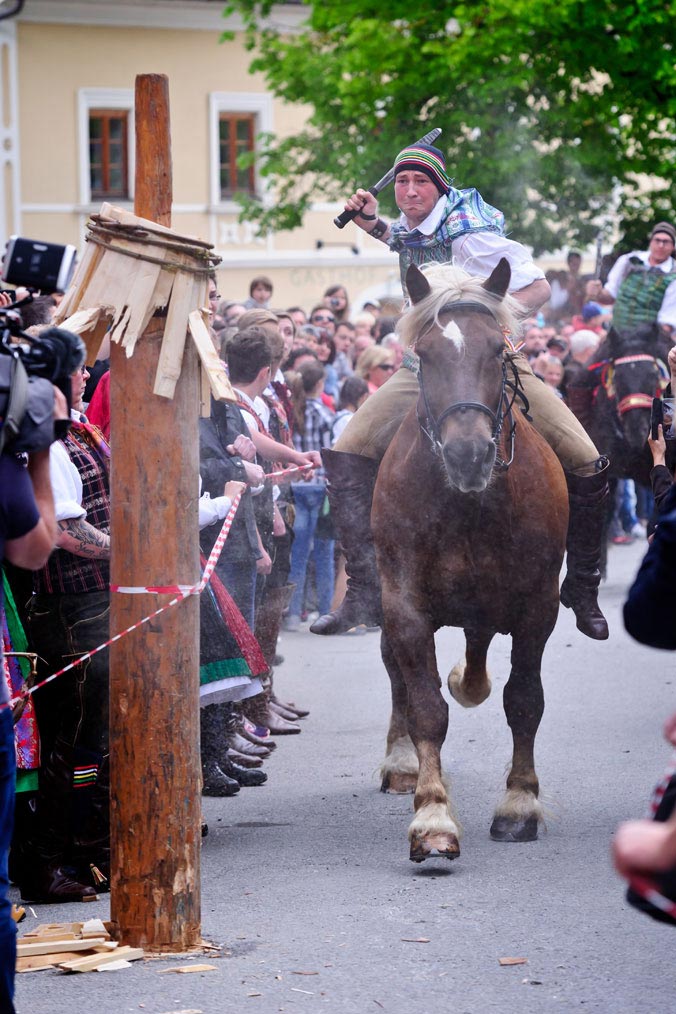 Mann auf Pferd reitet mit einer Keule in der Hand auf einen Holzpflock zu