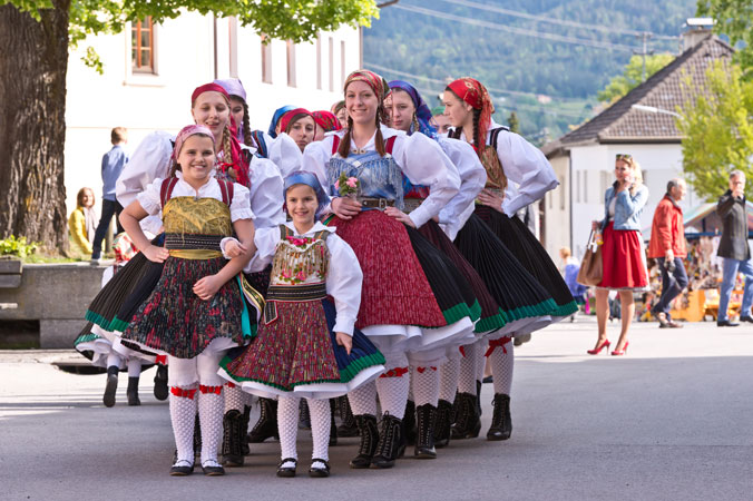 Beim Kufenstechen stehen junge Mädchen in Gailtaler Tracht in zwei Reihen auf einem Dorfplatz