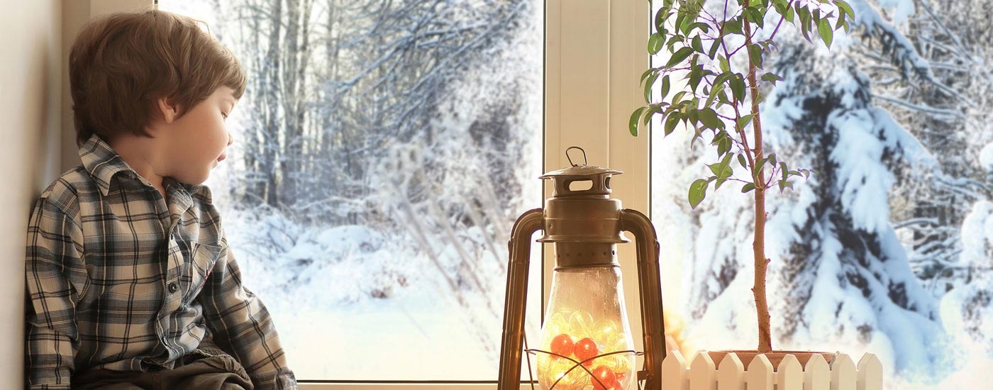 Warten - Junge sitzt am Fenster und schaut auf verschneite Winterlandschaft