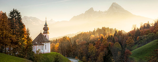 Eine Kapelle befindet sich vor einer bewaldeten Bergkulisse in der Dämmerung