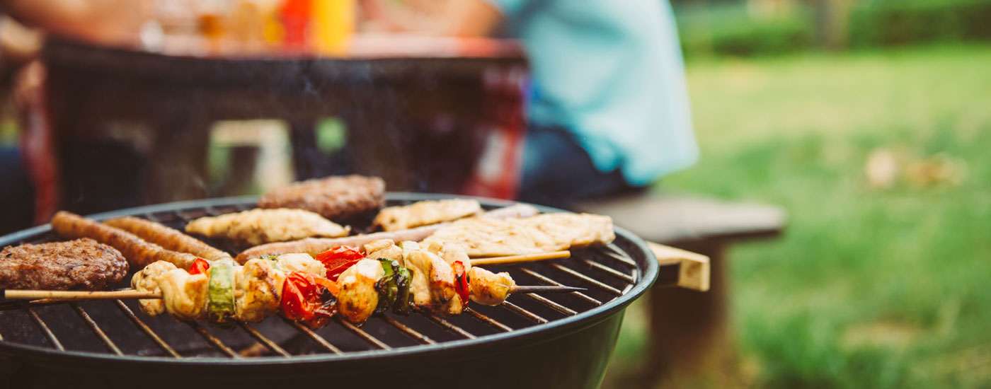 Ein Grill mit Fleisch und Spießen im Vordergrund, eine Gruppe von Menschen im Hintergrund