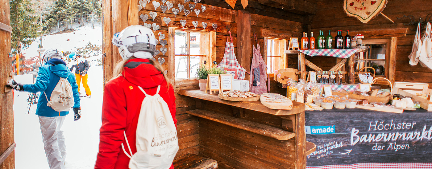 Ein Marktstand im Vordergrund, im Hintergrund Schnee: Besucher des Alpenbauernmarkts Radstadt Veranstaltungstipps März: Der höchstgelegene Bauernmarkt der Alpen